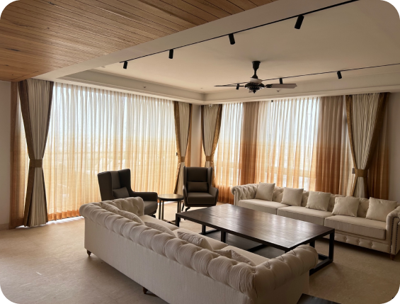 An Indian living room with sheer curtains and a city view beyond.